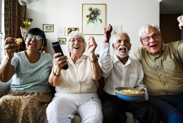 Group Of Cheerful Senior Friends Sitting And Watching TV Together