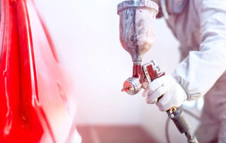 Close Up Of Spray Gun With Red Paint Painting A Car In Special Booth