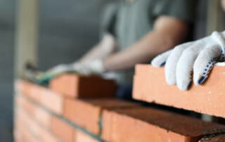 Two Workers Making Red Brick Wall At Construction Site Close Up